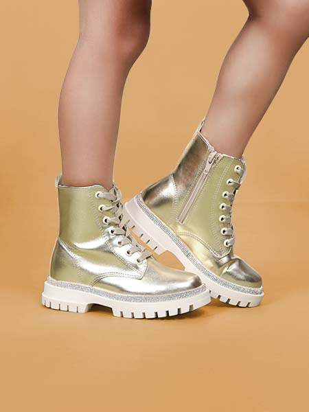 Zoom in a piernas de niña utilizando botas altas de cordones color dorado en fondo naranja